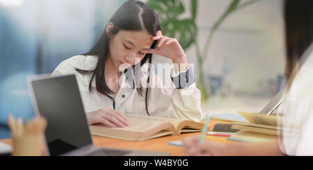 Adorabili Asian adolescente a studiare con un amico in biblioteca scolastica con sfondo sfocato Foto Stock