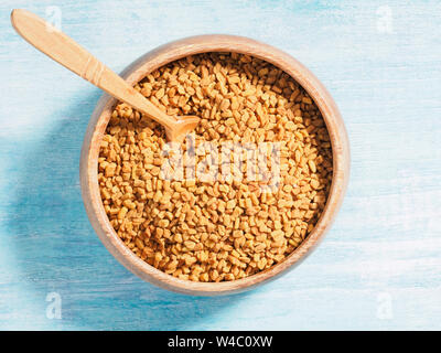 Spice Fieno greco (Trigonetla) in una coppa di legno su un blu e sfondo bianco con cucchiaino Foto Stock