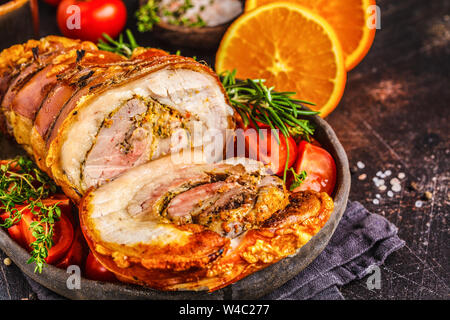 Classico italiano porchetta al forno con le arance. Carne di maiale cotta su uno sfondo scuro. Cucina Italiana concetto. Foto Stock