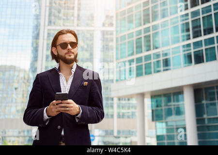 Foto del giovane uomo con la barba guardando al lato in città contro lo sfondo di edifici alti Foto Stock