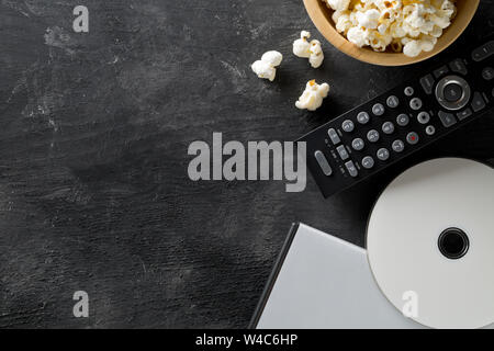 DVD o Blu-ray Disc con il telecomando del televisore e una ciotola di popcorn su sfondo scuro. Sistema home theater film o serie concetto di notte. Appartamento laici vista superiore Foto Stock
