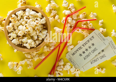 Biglietti per il cinema, soda drink cannucce di plastica e pop-corn giallo su sfondo tabella. Sistema home theater film o serie concetto di notte. Flat Top laici vista da ab Foto Stock