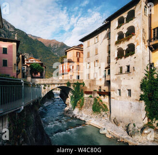 Vista panoramica sul piccolo fiume che scorre nella gola fra due case nella bella città di Chiavenna, Italia. Foto Stock