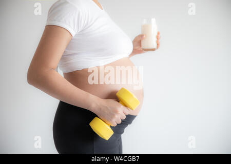 donna incinta e pesi dumbbell esercizio di formazione con un bicchiere di latte Foto Stock
