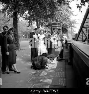 Un'annata di scena sul terrapieno a Londra come una folla si raduna attorno a un marciapiede artista al lavoro con il suo chalk negli anni cinquanta Foto Stock