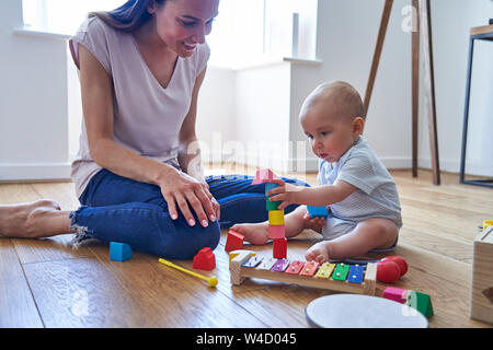Madre con 8 mese vecchio Figlio bambino imparare giocando con i colori dei blocchi di legno a casa Foto Stock