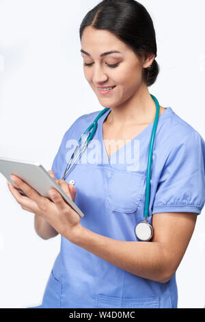 Studio shot di infermiera femmina indossando Scrubs utilizzando tavoletta digitale Foto Stock