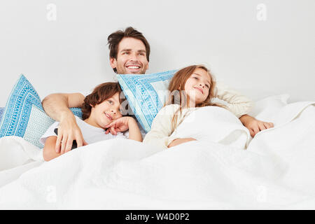 Padre Felice e i due ragazzi insieme guardare la TV a letto Foto Stock