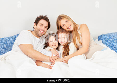 Genitori felici e due bambini Coccole a letto in camera da letto Foto Stock