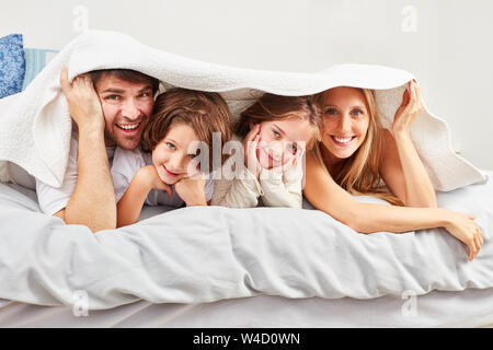 I genitori e i due bambini a nascondersi nella camera da letto sotto le coperte al mattino Foto Stock