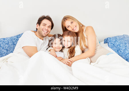 Genitori felici con due bambini al mattino insieme nel letto matrimoniale in camera da letto Foto Stock