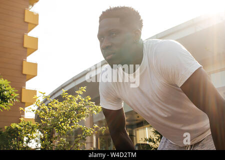 Ritratto di African American uomo di prendere un periodo di riposo durante il jogging. Giovane maschio montare persona fare esercizio e prendendo una pausa nel parco della città Foto Stock