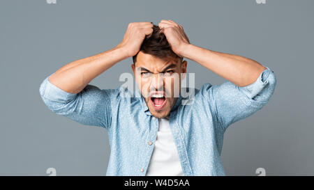 Frustrati Guy tirando i suoi capelli fuori su grigio di sfondo per studio Foto Stock
