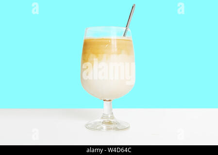 Iced latte caffè su un bianco tavolo di legno contro un semplice sfondo teal. Il caffè bevanda di latte e svuotare lo spazio di copia per l'editor di testo. Foto Stock