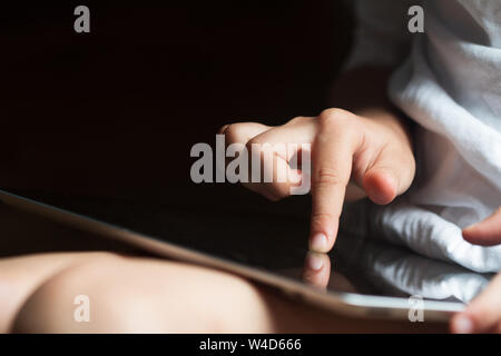Primo piano vista frontale del bambino caucasico mano toccando lo schermo di un computer tablet in condizioni di luce diurna Foto Stock