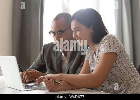 Felice diversi colleghi discutere il lavoro online utilizzando computer portatile in ufficio Foto Stock
