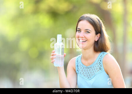 Donna felice tiene una bottiglia di acqua guardando la fotocamera su sfondo verde Foto Stock