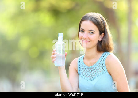 Donna sorridente tenendo una bottiglia di acqua guardando la fotocamera su sfondo verde Foto Stock