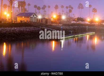 Mattinata nebbiosa attenua la luci riflettente sulla superficie liscia della Ocean Cove dock l'acqua. Foto Stock