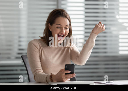 Euforico giovane imprenditrice vincitore utilizza lo smartphone celebrare win mobile Foto Stock