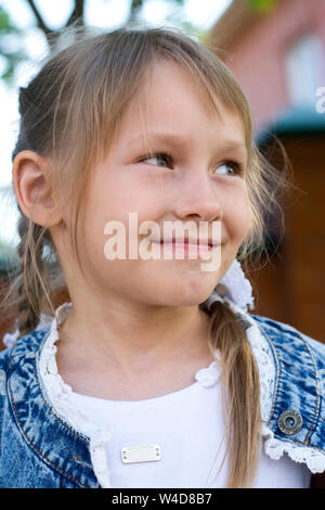 Una ragazza con una spiralina in una camicia di denim e abito bianco passeggiate al tramonto nel parco. Foto verticale Foto Stock