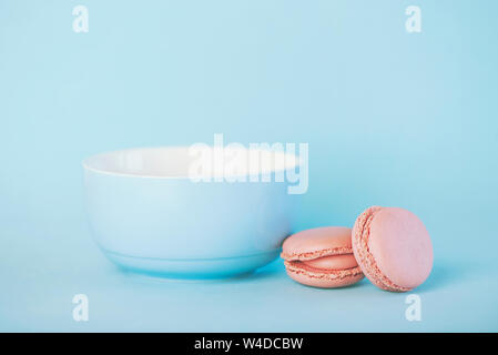 Lampone rosa pastello macarons accanto a un vaso blu su sfondo blu Foto Stock