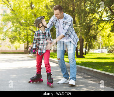 Felice ragazza nel casco di pattinaggio di apprendimento con suo padre Foto Stock