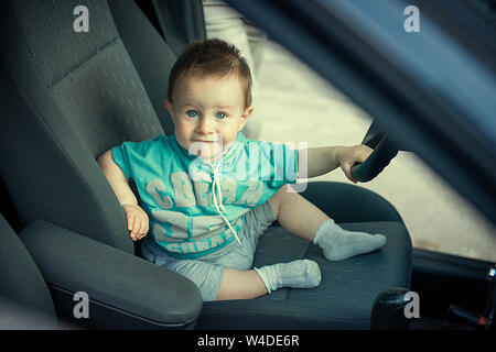 Un anno e mezzo di lavoro vecchio bambino si siede dietro al volante di una vettura Foto Stock