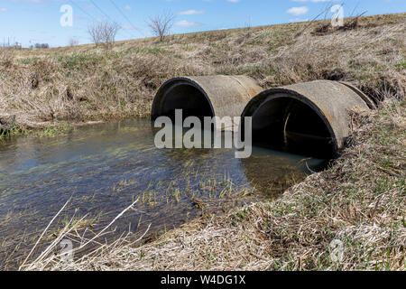 Storm runoff di acqua che fluisce dalla fossa di scolo in concrete condotte sotto una strada Foto Stock