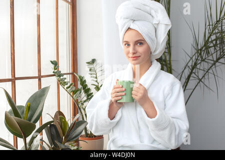 Giovane donna alla casa di cura di bellezza in piedi tenendo tazza di tè positivo sorridente Foto Stock
