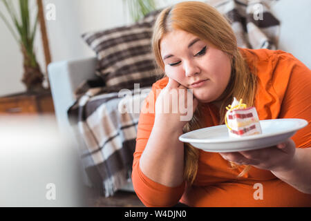 Chubby donna lo sport a casa seduti guardando torta sconvolto Foto Stock