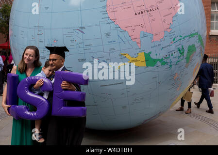 Sotto la scultura da Turner Prize-winning artista Mark Wallinger intitolata " Il mondo Capovolto', neolaureati subito dopo il loro cerimonie di laurea incontrare la famiglia e gli amici al di fuori della London School of Economics (LSE), il 22 luglio 2019, a Londra, in Inghilterra. " Il mondo Capovolto' è un grande globo politico, di quattro metri di diametro con gli Stati nazione e i confini delineati ma con il semplice e rivoluzionario di torsione essendo invertito. La maggior parte delle landmasses giacciono ora nel 'inferiore' emisfero con i paesi e le città di re-etichettati per questo nuovo orientamento. Foto Stock