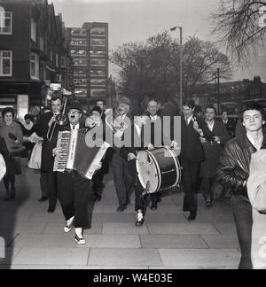 Anni sessanta, storico, commedia stelle del pannello della radio gioco, "La squadra pensa a piedi verso il basso a South London street in serata, giocando muscial come strumenti di promozione per il gioco, Londra, Inghilterra, Regno Unito. Il popolare gioco del pannello, una parodia di " Domande " è stato svolto per la ride e ha funzionato per quasi vent'anni. Foto Stock