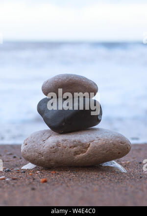 Una piccola collezione di pietre impilate sulla spiaggia con l'oceano sullo sfondo Foto Stock