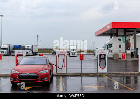 Tesla Model S inserito, sovralimentando con stazione di gas in background. Foto Stock