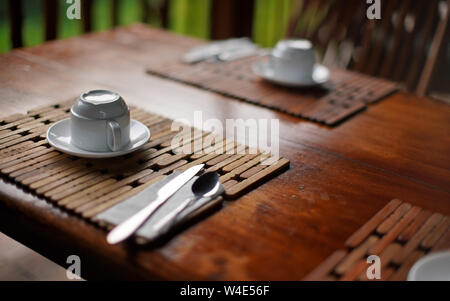 La profondità di campo di una foto di dettaglio del vuoto tazza da caffè capovolta sul tavolo in legno scrivania, prima colazione al mattino nel tropical holiday resort Foto Stock