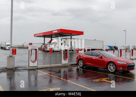 Tesla Supercharger stazione con il modello rosso S carica, carrello-stop in background. Foto Stock