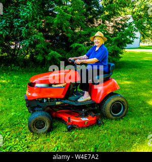 Donna anziana prato falciatura sul suo trattore in un giorno d'estate. Foto Stock