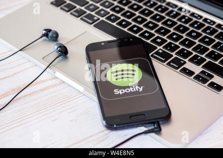 Nizhyn, Ucraina/Luglio-16-2019: Smartphone con Spotify app Musica e cuffie giacente sul laptop Macbook Foto Stock