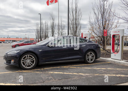 Blu modello Tesla S parcheggiato a Tesla Supercharger in Markham, su con il modello S, modello X e bandiera canadese in background. Foto Stock