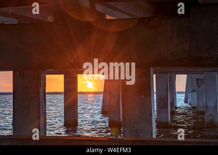 Vista del sole nascente sotto il ponte sopra l'acqua Foto Stock