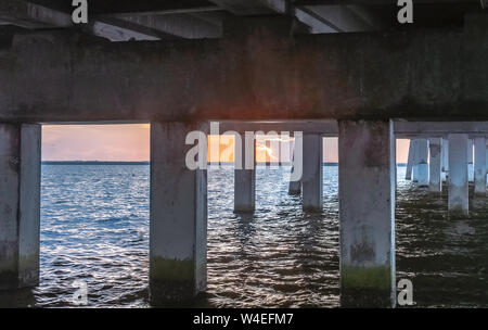 Vista del sole nascente sotto il ponte sopra l'acqua Foto Stock