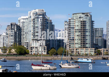 Barche nel porto di Vancouver, False Creek con condomini e montagne coperte di neve sullo sfondo. Foto Stock