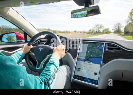 Uomo alla guida di Rosso Modello Tesla S con navigazione sullo schermo accanto. Interno rivestito in bianco e nero e in pelle grigia. Foto Stock