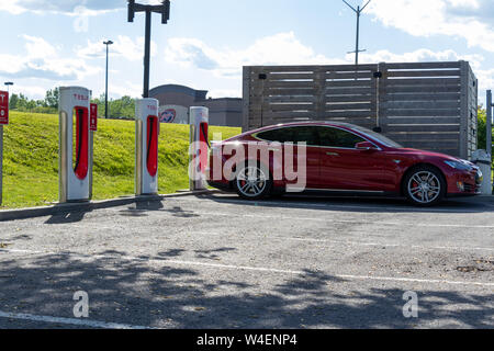 Rosso Modello Tesla S carica a un sovralimentatore di Tesla in Cornovaglia, Ontario in una giornata di sole. Foto Stock