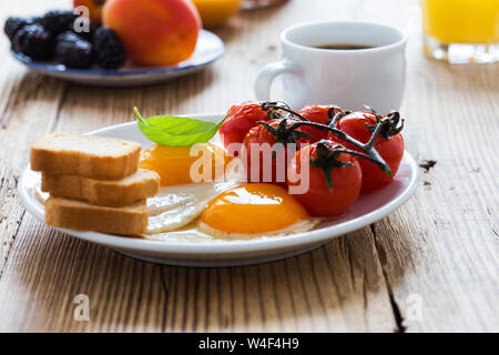 Una sana colazione vegetariana o il brunch, cibo preferito. Uova fritte con pomodori ciliegia, freschi frutti estivi, bacche, caffè e succo di frutta, rustico woo Foto Stock