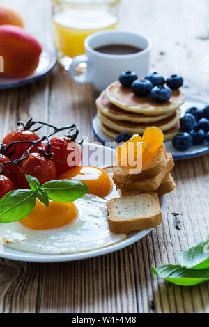 Una sana colazione vegetariana o il brunch, cibo preferito. Uova fritte con pomodorini, frittelle, fresca estate frutti, bacche, caffè e succo di frutta, a Foto Stock