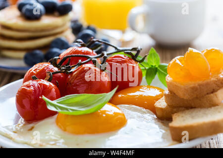 Una sana colazione vegetariana o il brunch, cibo preferito. Uova fritte con pomodorini, frittelle, fresca estate frutti, bacche, caffè e succo di frutta, a Foto Stock