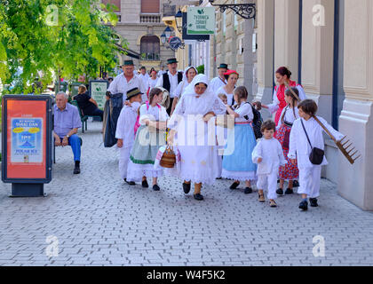 Zagabria, Croazia. Gruppo di persone vestite di bianco abiti tradizionali camminando sulla strada della città con le attività agricole e le attrezzature di cottura. Foto Stock