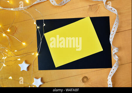 Mockup Natale foglio di colore giallo con scatola xmas ghirlanda dorata su sfondo di legno. Vista superiore per il biglietto di auguri con il luogo per il testo Foto Stock